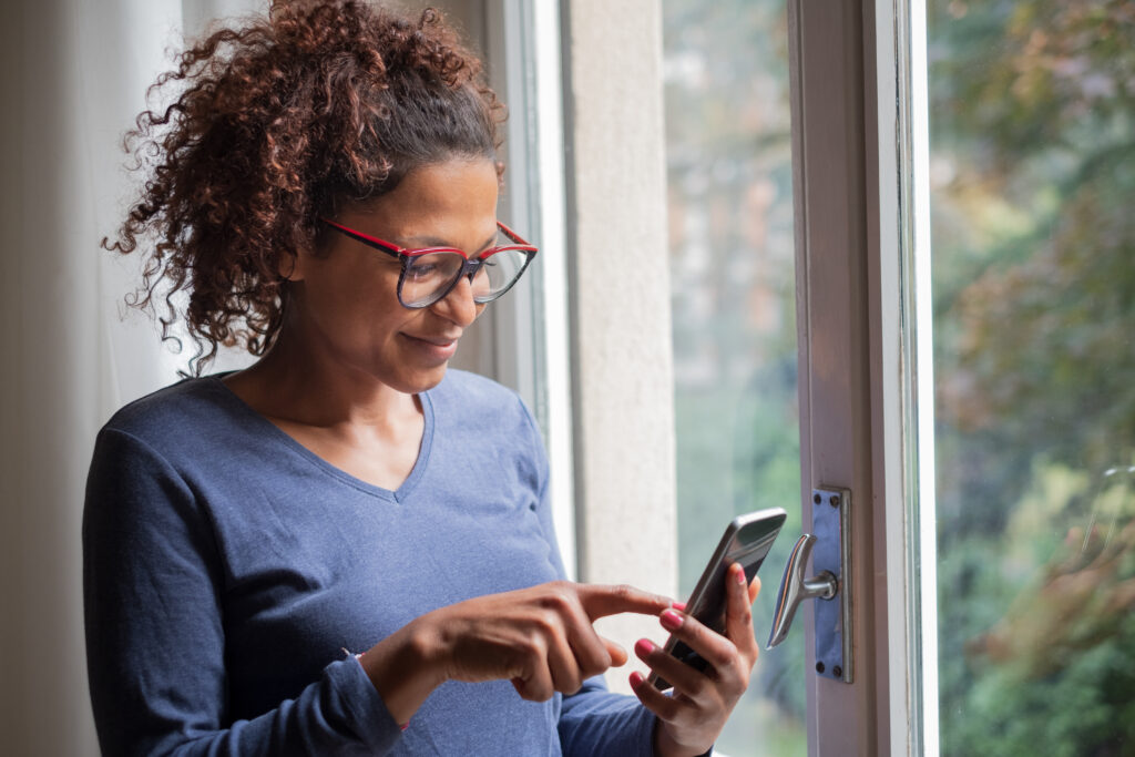Why Women In Midlife Need Each Other…And A Menopause Specialist 1 When To Talk To A Menopause Specialist -- Photo Of Smiling Black Woman Standing Beside Window Researching On Her Phone