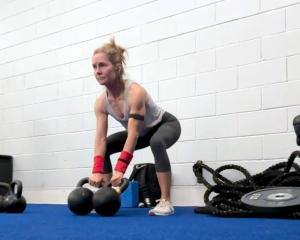 Adrien Cotton In A Gym In A Low Squat, Ready To Swing Two Kettlebell Weights.