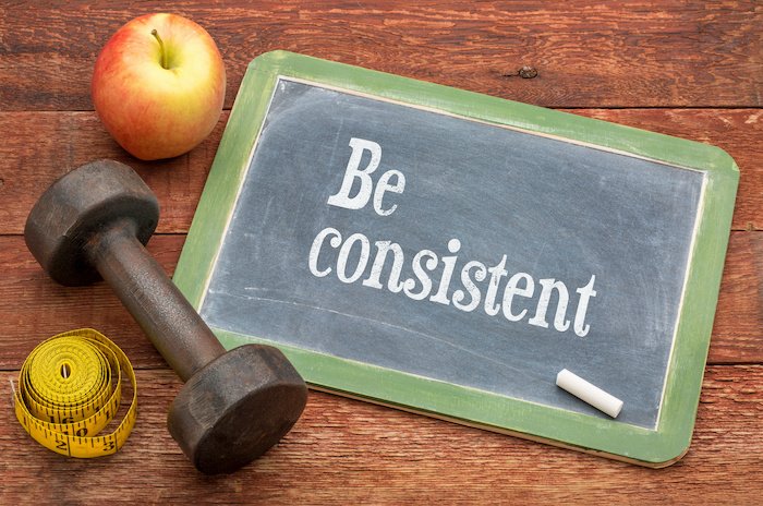 Be Consistent Written On A Chalkboard Next To A Weight And An Apple