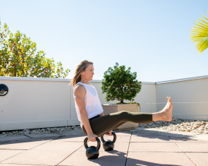 Adrien Cotton balances in a pike position with legs extended on two kettlebells.