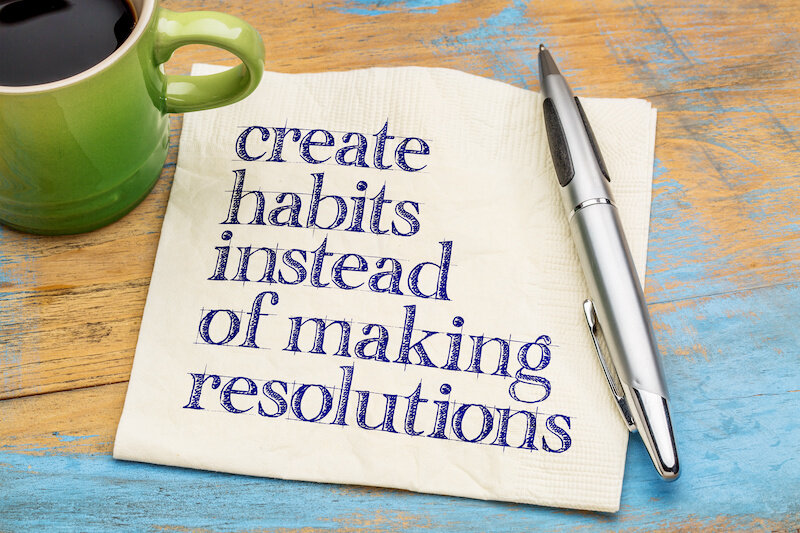 The Quote 'Create Habits Instead Of Resolutions' - On A Napkin With A Cup Of Coffee