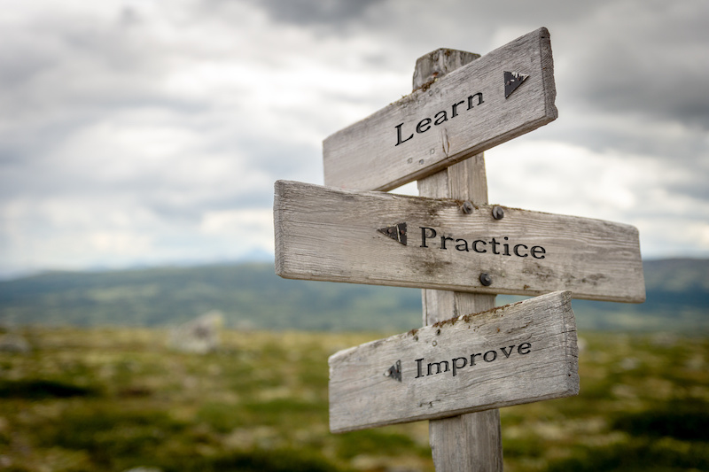 Wooden Sign Post Outside That Says Learn, Practice, Improve