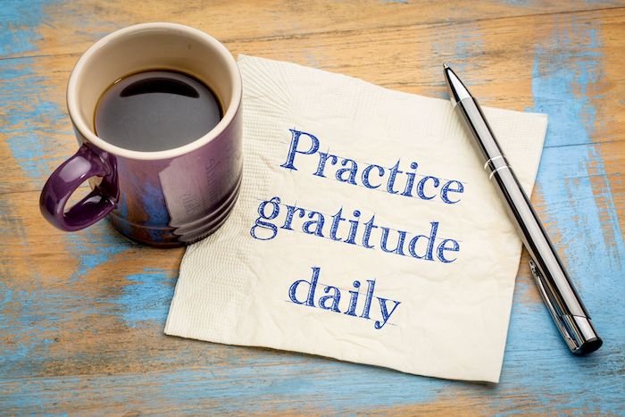 Practice Gratitude Daily Written On A Napkin Next To A Pen And Coffee Cup