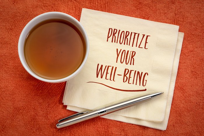 Prioritize Your Well Being Written On A Napkin With A Cup Of Coffee And Pen