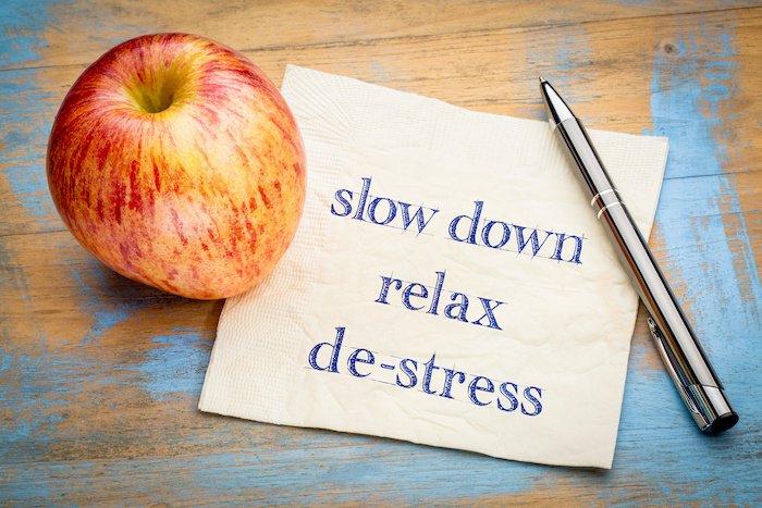 Napkin With The Words Slow Down, Relax, De-Stress Next To A Pen And An Apple