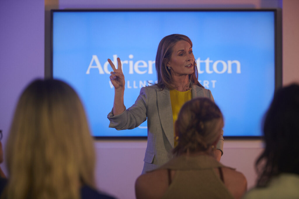 Adrien Cotton Speaking In Front Of A Corporate Audience, Holding Up Two Fingers