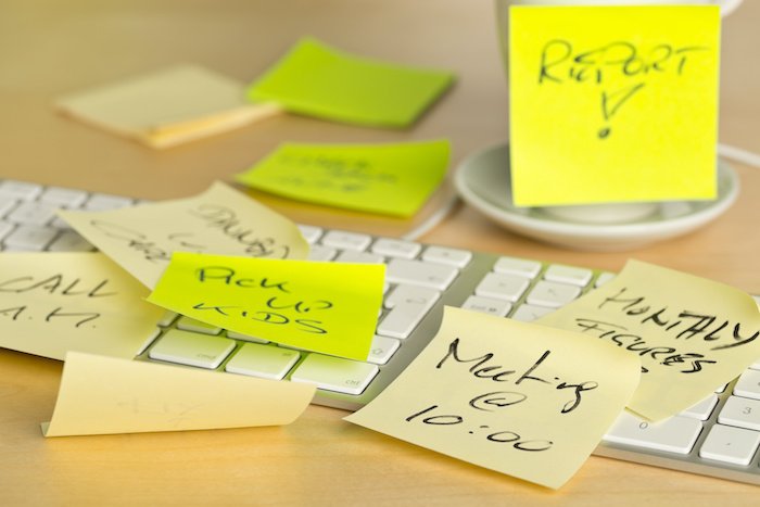 Computer Keyboard And Coffee Cup Covered With Sticky Notes With Different Appointments On A Wooden Desk