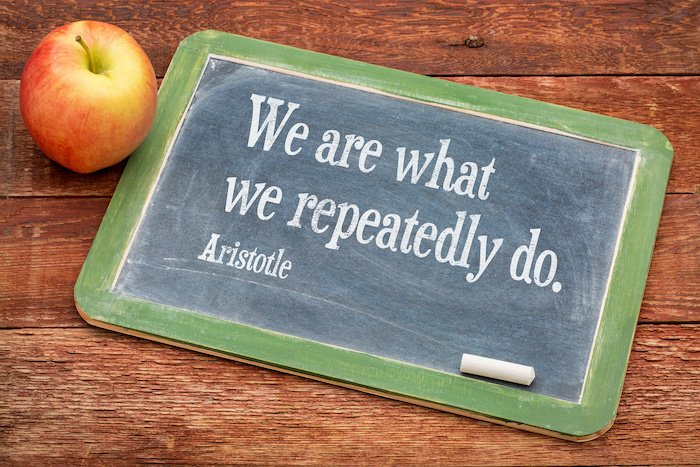 We Are What We Do - Aristotle Quote On A Slate Blackboard On A Wooden Table Next To An Apple