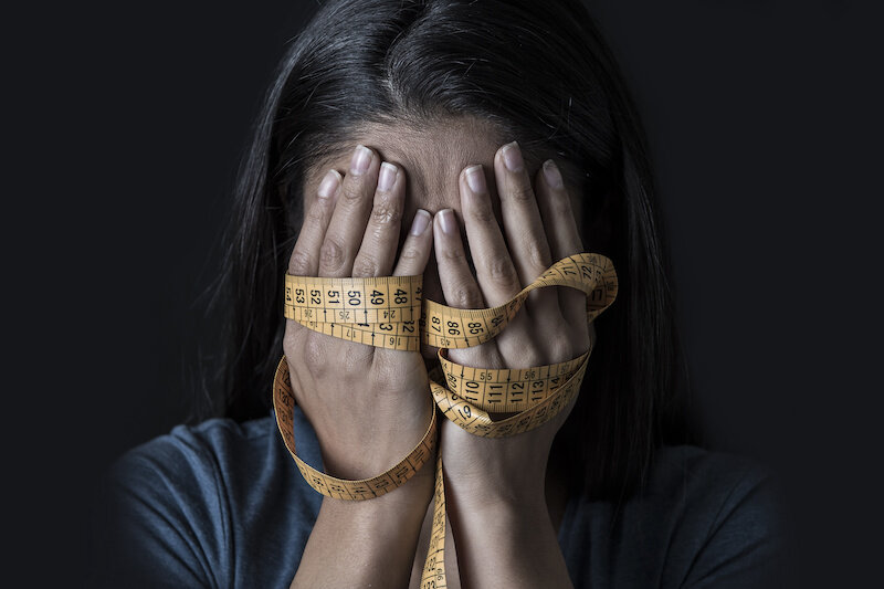 Close Up Hands Wrapped In A Measuring Tape Covering Face Of Young Depressed And Worried Woman.