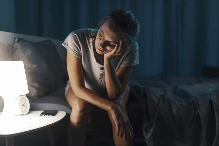 Exhausted Woman Suffering From Insomnia Caused By Perimenopause Sitting On The Edge Of Her Bed