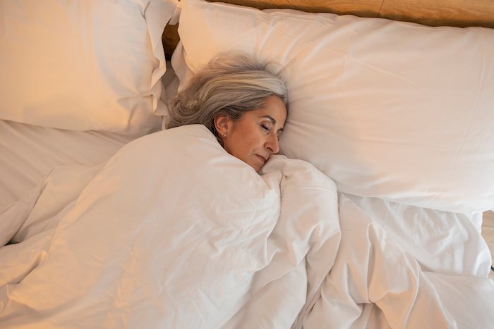 Mature Woman Sleeps In A Bed With White Bedding