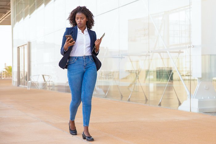 Black Business Woman Walking Outside Looking At Her Phone.