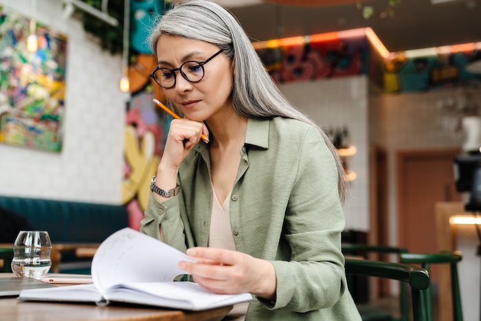 Mature Woman Thinking Over A Notebook At A Table.