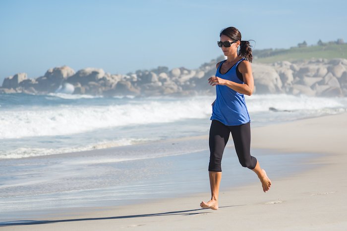 Woman Running On The Beach With A Blue Shirt And Black Leggings.