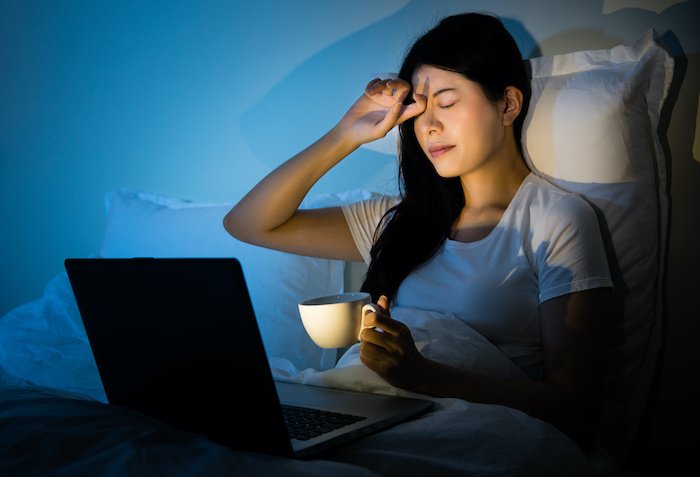 Woman In Bed With A Laptop And Coffee Rubbing Her Eyes