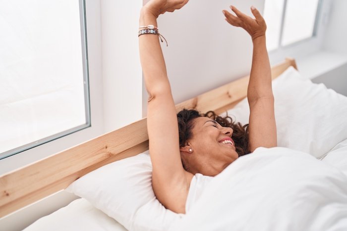 Middle Age Woman Waking Up Stretching Arms At Bedroom