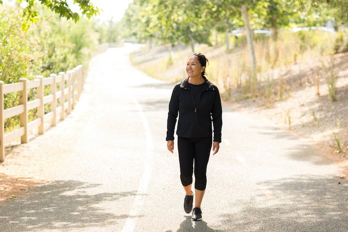 Portrait Of A Fit Asian Woman Walking Outside On A Road On A Sunny Day.