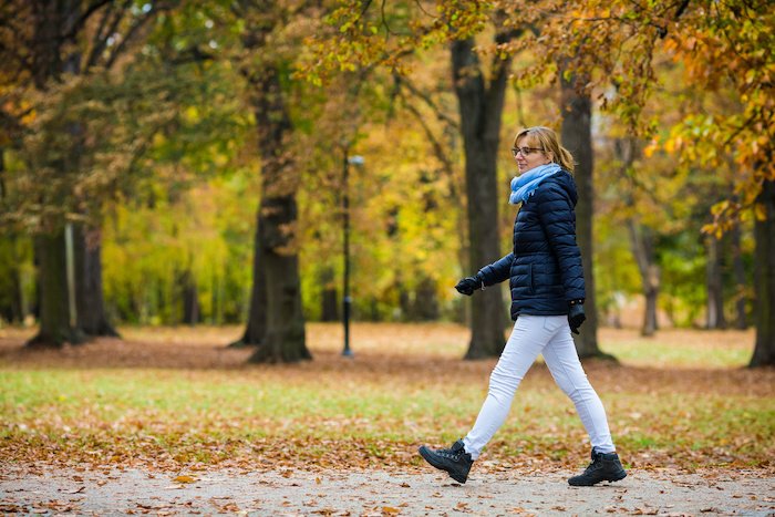 Middle Aged Woman Taking A Walk Outside With Fall Leaves And Winter Coat