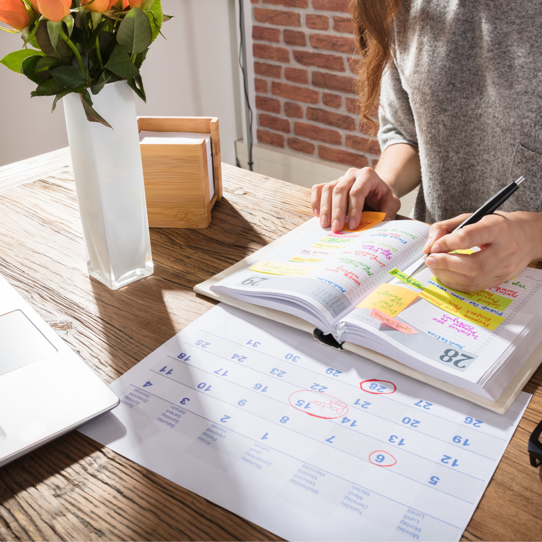 woman in a gray sweater writing in her daily planner at a wooden desk with flowers